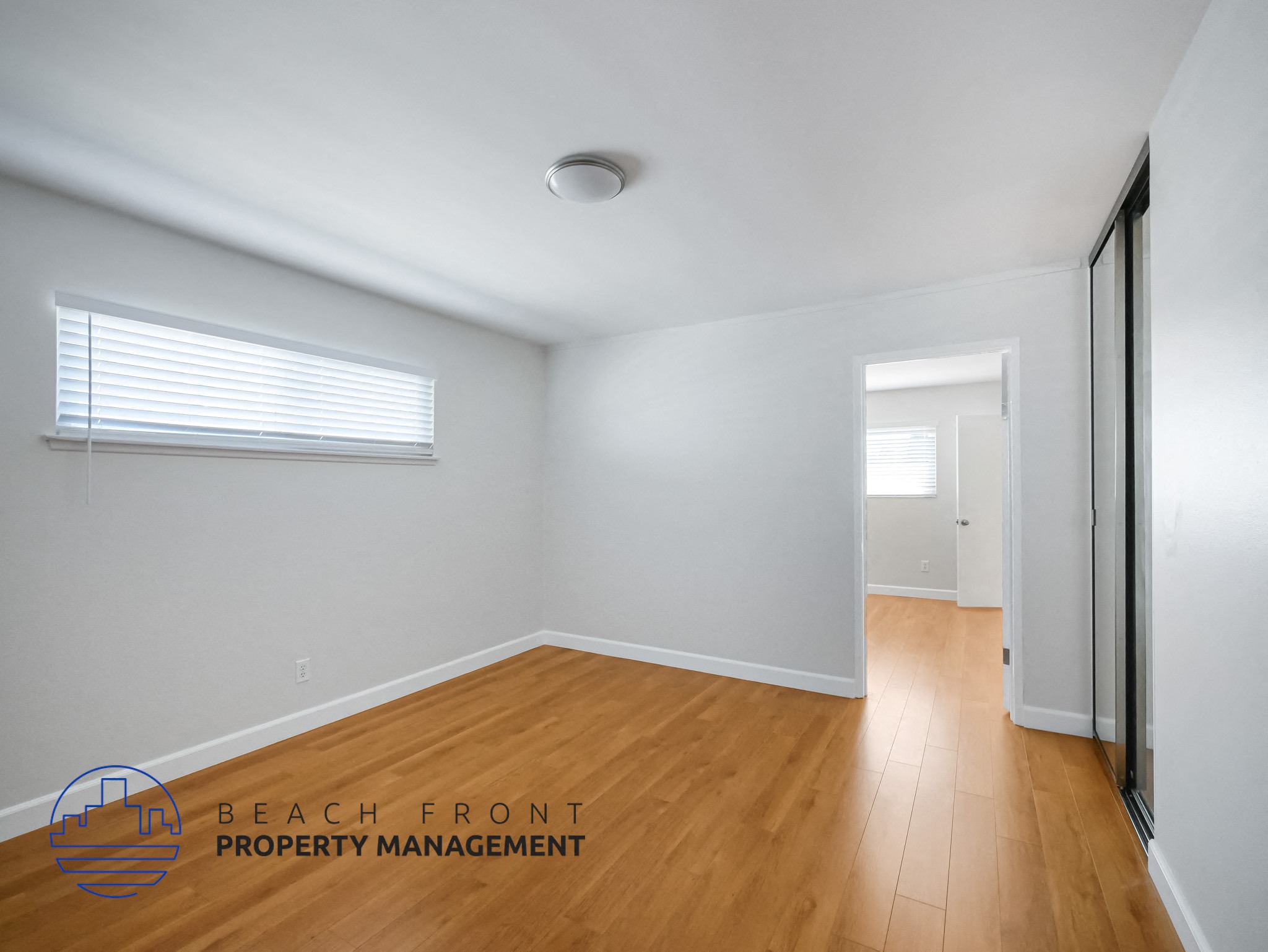 A room with wooden floors and white walls, with a window and a door visible.
